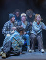 6 people sat on bench on stage lit.